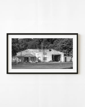 Black and white photograph of an abandoned Indiana service station and garage surrounded by trees.