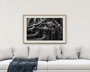 Dense industrial pipework with curved elbows and rows of bolts photographed in monochrome.
