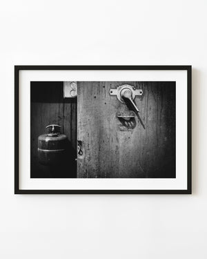 Black and white close-up of a machine lever on a weathered metal panel with strong angled shadows.