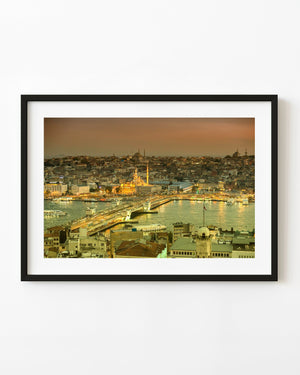 Galata Bridge and Istanbul’s waterfront glow at dusk beneath an orange sky, with boats on the water.