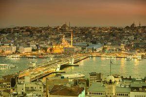 Elevated evening view of Istanbul with Galata Bridge, illuminated mosques and ferries along the waterfront.