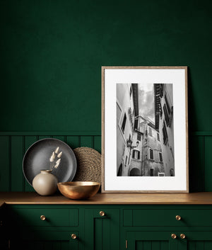 Italian alley architecture with layered windows and lanterns beneath an opening of cloudy sky.