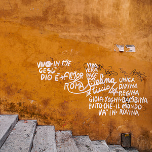 Three closed shop doors with graffiti along an old Roman street wall