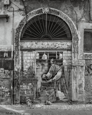 Street art painting on closed storefront door beneath arched window Italy
