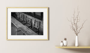 Rustic wooden chairs lined against textured wall in monochrome