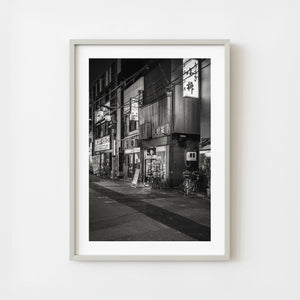 Monochrome Tokyo street at night with storefronts and bicycles