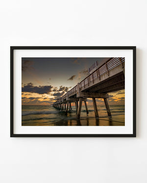 Juno Beach pier stretching into the ocean beneath a golden sunrise