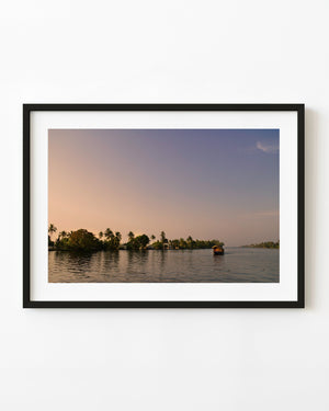 Boat crossing Kerala’s backwaters beneath a warm sunset sky