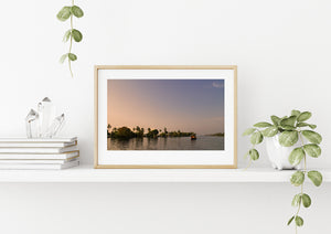 Colour photograph of a boat and palms beneath a pastel evening sky
