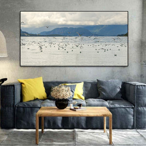 Seabirds scattered across pale water beneath distant green mountains