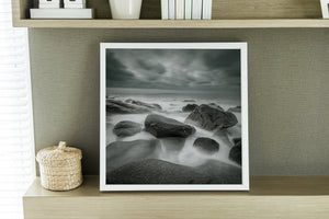 Textured Kostbergan boulders contrast with silky water in a subdued coastal landscape.