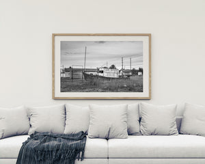 Tall grasses surround an old fishing boat beneath utility wires and cloudy sky.
