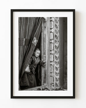 young Tibetan monk looking from monastery window Larung Gar China black and white