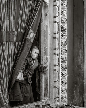 child monk standing in doorway curtain Larung Gar Buddhist monastery