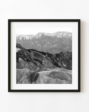 Layered rocky mountain ridges with distant snow-covered peaks in black and white.