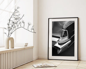 Framed black and white car portrait on a wall in a room with a radiator and plant.