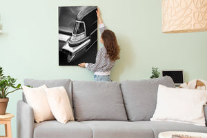 Woman hanging a large black and white photograph of a classic car on a light green wall above a gray sofa.