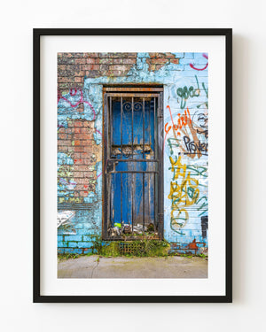 Weathered blue London door behind an iron gate, surrounded by graffiti and exposed brick