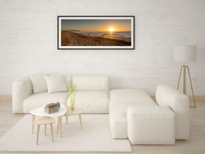 Golden sun above ocean waves and people walking at the waterline
