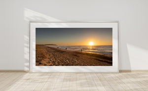 Long Reef Beach at sunrise with a headland, sandy shore and small human figures
