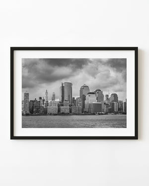 Lower Manhattan waterfront skyline beneath heavy clouds in black and white