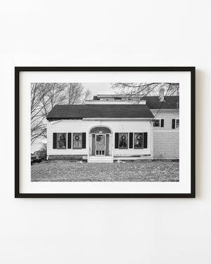 Black and white photograph of a Maine house with an American flag across the front door