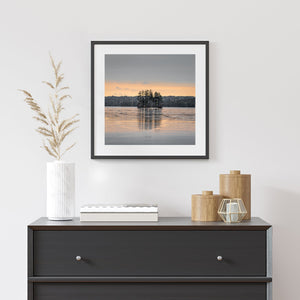 Pine-covered Maine island reflected in peach twilight on calm water