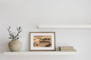 A man walks past stone and earthen walls beside a house with green doorway fabric