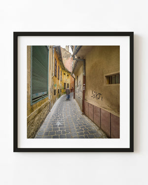 Man carrying a bag walks through a narrow cobblestone lane in Brașov, Romania