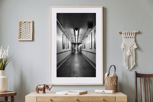 A lone man walks between converging walls in a long station passage