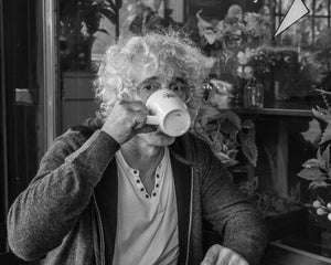 Person with curly hair and glasses sipping coffee beside a Manhattan café window