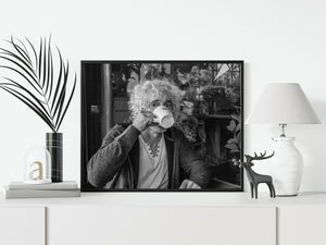 Black and white photograph of a coffee drinker framed by café plants and glass
