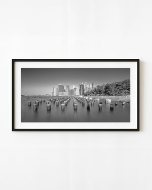 Black and white Manhattan skyline beyond rows of waterfront pilings