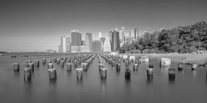 Long exposure view of Lower Manhattan across smooth water and old pier posts