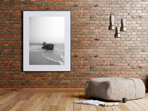 Monochrome seascape of waves sweeping across sand around two coastal boulders