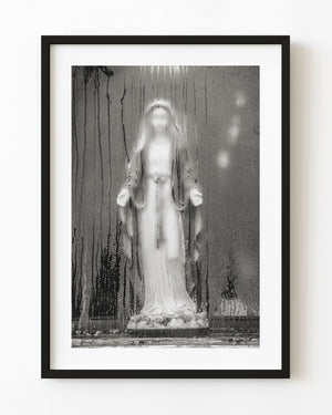 Black and white photograph of a Mary statue behind steamed glass