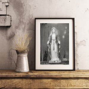 A white Mary statue contrasts with dark streaks on a fogged window