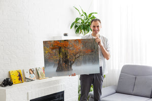Man holding a large canvas print of a nature scene in a living room.