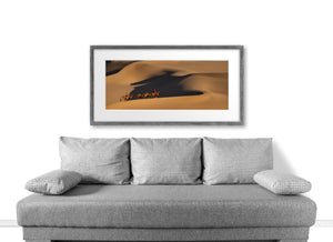 Panoramic Mongolian desert photograph with camel riders and layered golden dunes