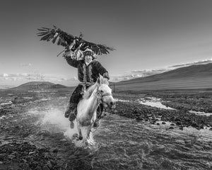 Black and white photo of Kazakh eagle rider crossing water on horseback