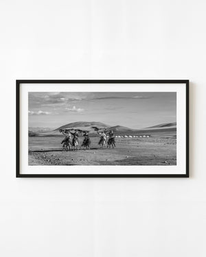 Mongolian eagle hunters on horseback raise their birds against open hills in black and white