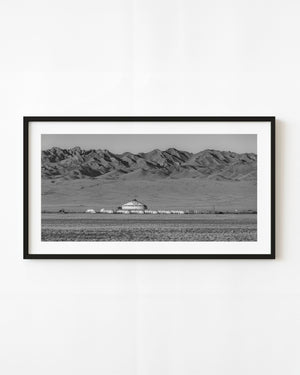 Black and white Mongolian yurt camp beneath a broad rugged mountain range