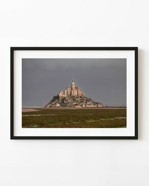 Sunlight illuminates Mont Saint-Michel abbey beneath a broad grey sky