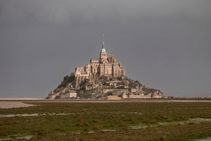 The island abbey rises above a green tidal foreground and fortified village