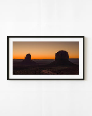 Monument Valley buttes silhouetted beneath a warm orange sunset sky