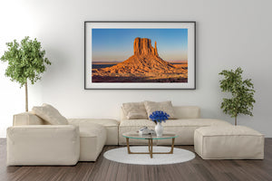 Long shadows cross the foreground beneath a brightly lit Monument Valley formation