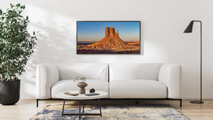 Rugged sandstone slopes and a narrow rock spire catch low golden light