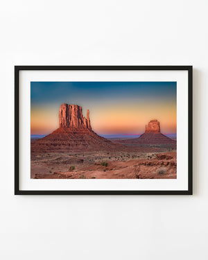 The Mittens in Monument Valley glow red beneath a pastel sunset sky