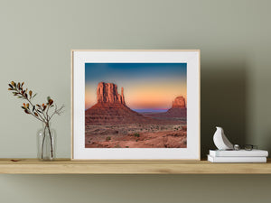 Layered red sandstone cliffs catch sunset light above scattered desert shrubs