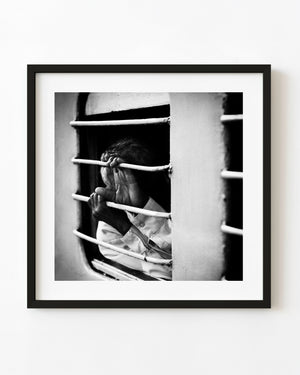 Black and white photograph of a train passenger covering their face behind a barred window in Mysore India